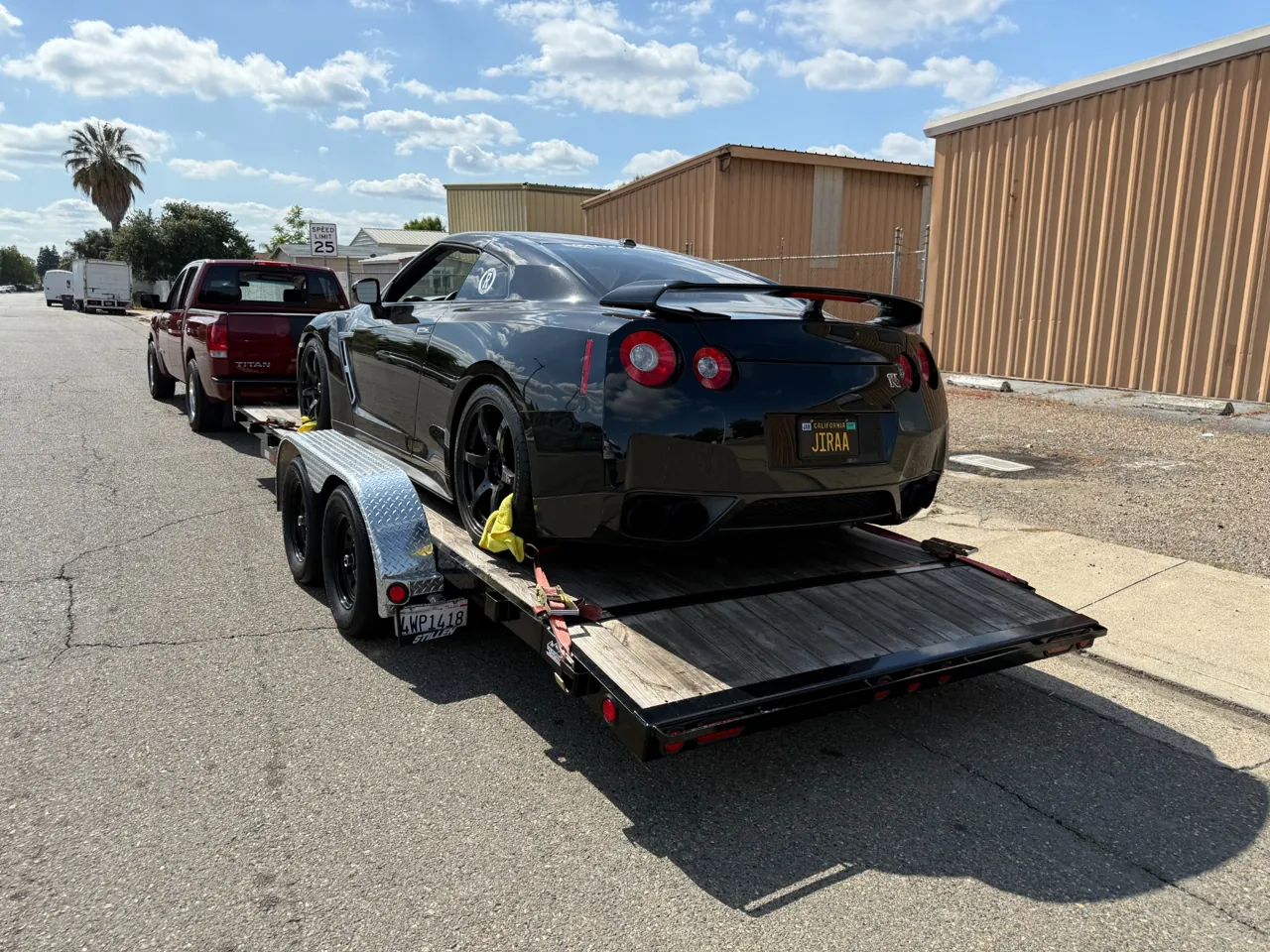 Black performance coupe on a trailer behind a pickup in daylight